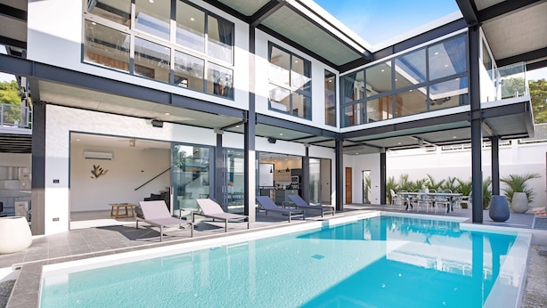 Et moderne hus med swimmingpool, glasdøre og udendørs møbler.