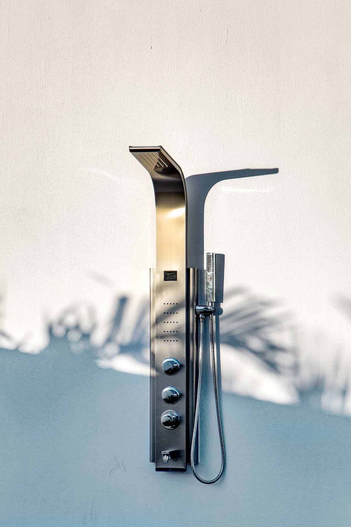 A metallic wall-mounted shower with a hose and control knobs.