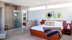 A modern bedroom with a large bed, a glass shower enclosure, a wooden nightstand, and a ceiling fan. - Luxury 3bdr Villa with Private Pool, Oceanview and Hotel Amenities v4 (Providenciales)
