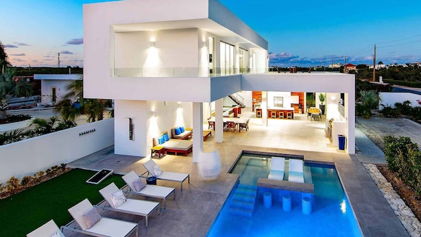 A modern two-story house with a swimming pool, outdoor seating, and a well-lit interior. - Luxury 3bdr Villa with Private Pool, Oceanview and Hotel Amenities v4 (Providenciales)