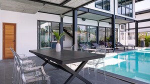 A modern indoor pool area with a glass table and chairs, a wooden door, and a staircase leading to upper levels. - Innovative 12m Eco Pool Villa Sunset 1 (Rawai)