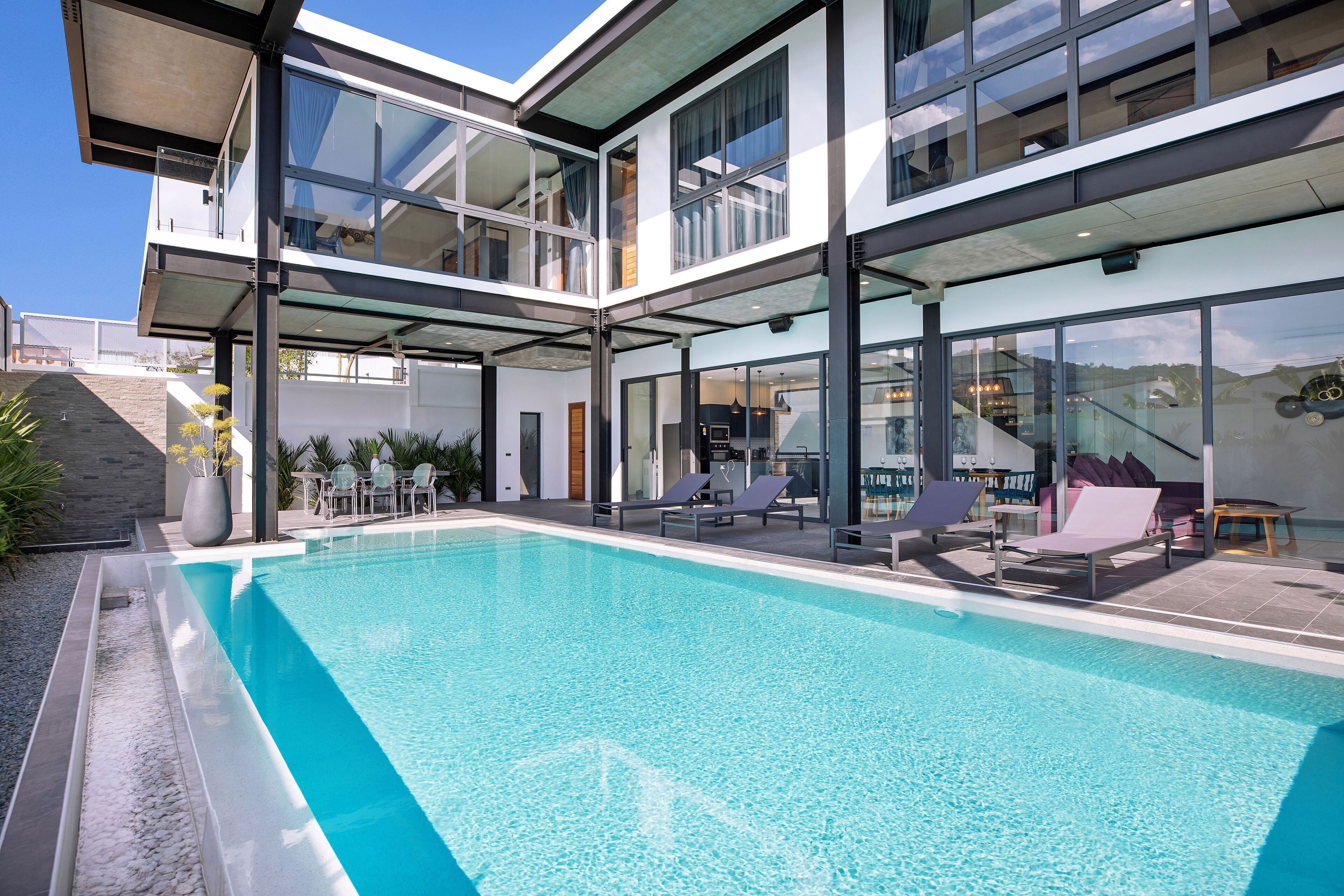 A modern house with a swimming pool, outdoor seating, and a large glass window.