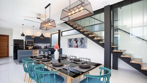 A modern kitchen with a dining area, featuring a staircase and a glass wall. - Innovative 12m Eco Pool Villa Sunset 1 (Rawai)