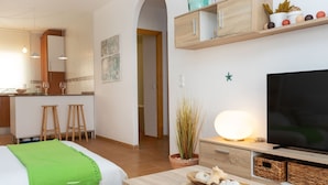 Et moderne hotelværelse med en seng, et fjernsyn, et træskrivebord og et tekøkken i baggrunden.