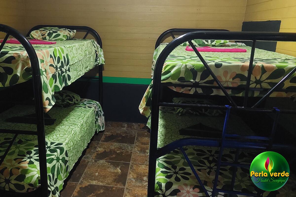 Une chambre d’auberge de jeunesse avec des lits superposés, chacun étant agrémenté d’une couverture et de coussins à motifs. La chambre a un sol carrelé et des murs en bois.