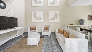 A living room with a TV, white wicker furniture, patterned floor, and wall art. - Bamboo Damai Villa by Betterplace (Kerobokan)