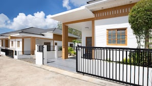 A residential building with a modern design, featuring a gated entrance, a covered walkway, and a well-maintained garden area. - Japanese Style Villa Sunrise Garden B190 (Thep Krasattri)