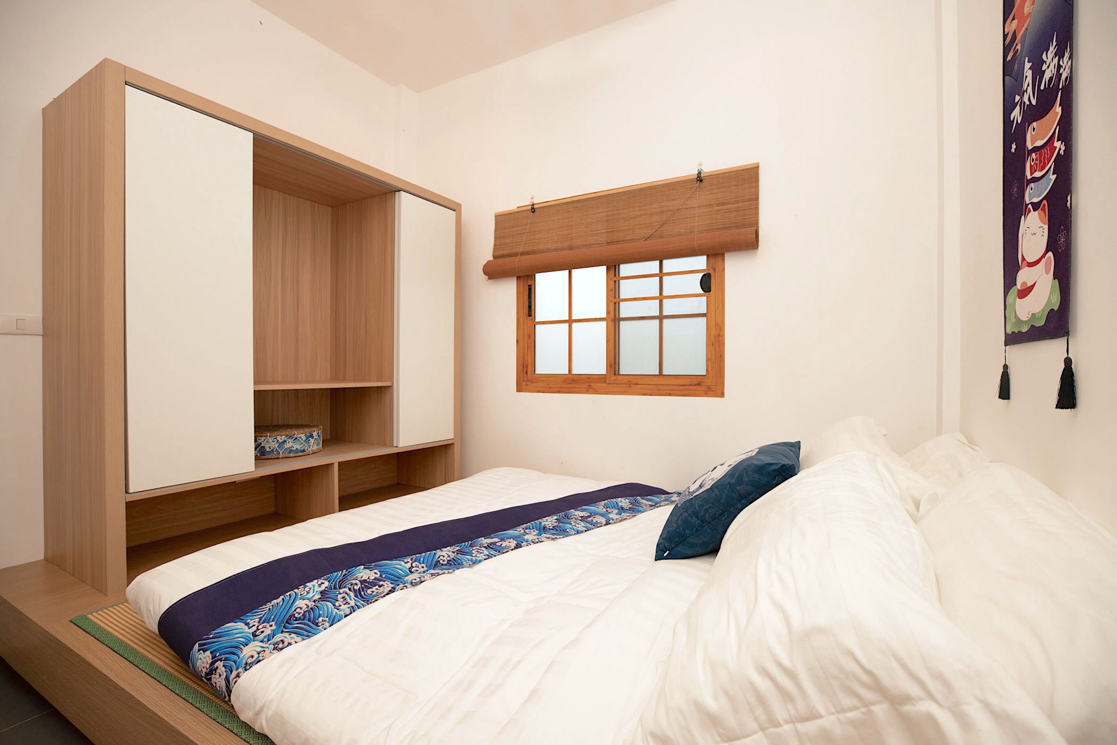 A bedroom with a bed, a wooden wardrobe, a window with a view, and a wall decoration.
