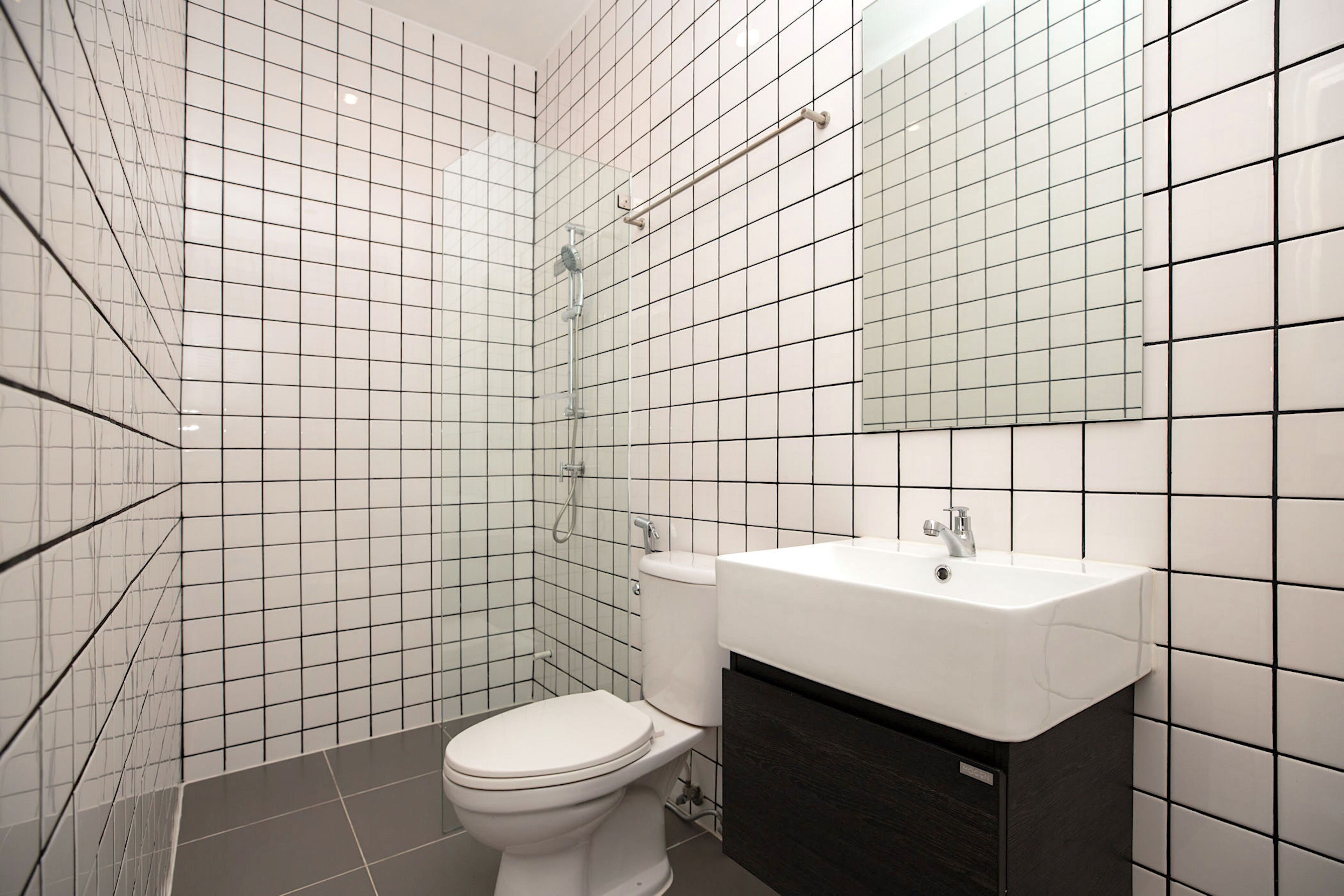 A bathroom with white tiled walls, a white toilet, a white sink, and a dark wooden cabinet.