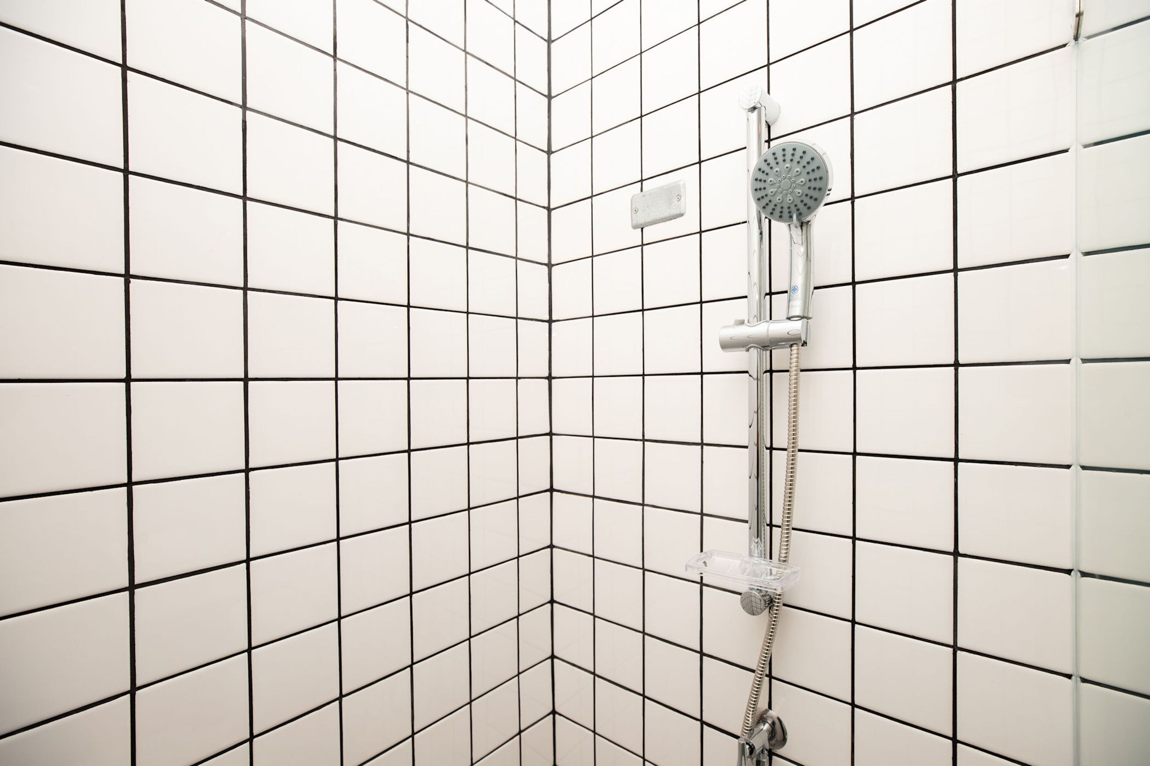 Un coin d’une pièce aux murs recouverts de carreaux blancs et dotée d’une douche.