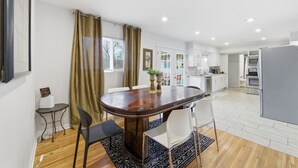 A modern kitchen with white cabinets, a grey refrigerator, and a dining area with a wooden table and chairs. - Near WSU:  Bumper Pool and Fire Pit! (Wichita)