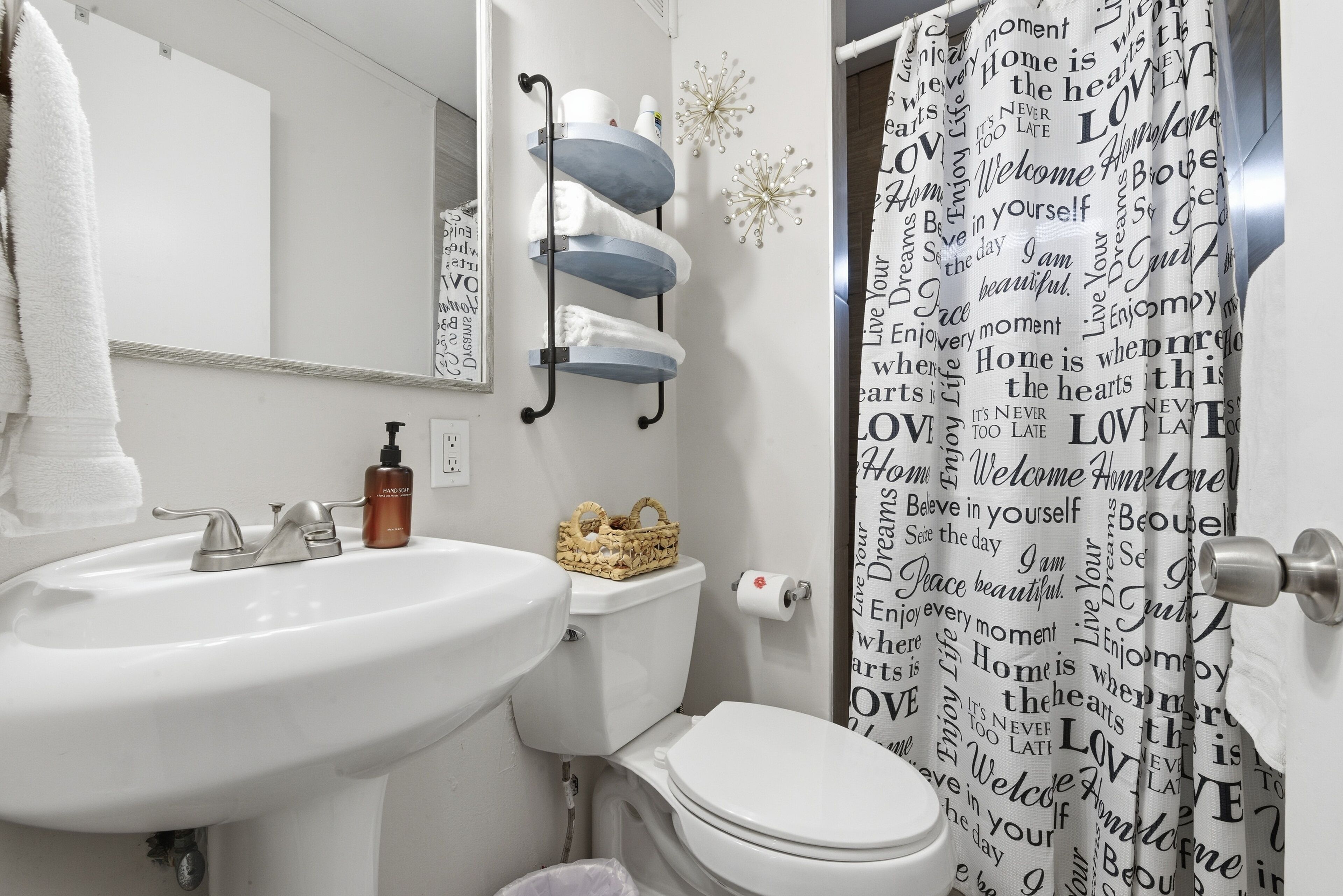 A bathroom with a white sink, a toilet, and a shower curtain with motivational words.