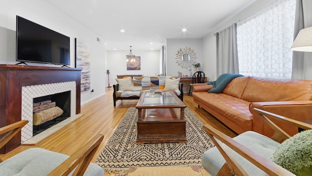 A modern living room with a fireplace, a large flat-screen TV, a brown leather sofa, a coffee table, and a patterned rug. - Near WSU:  Bumper Pool and Fire Pit! (Wichita)