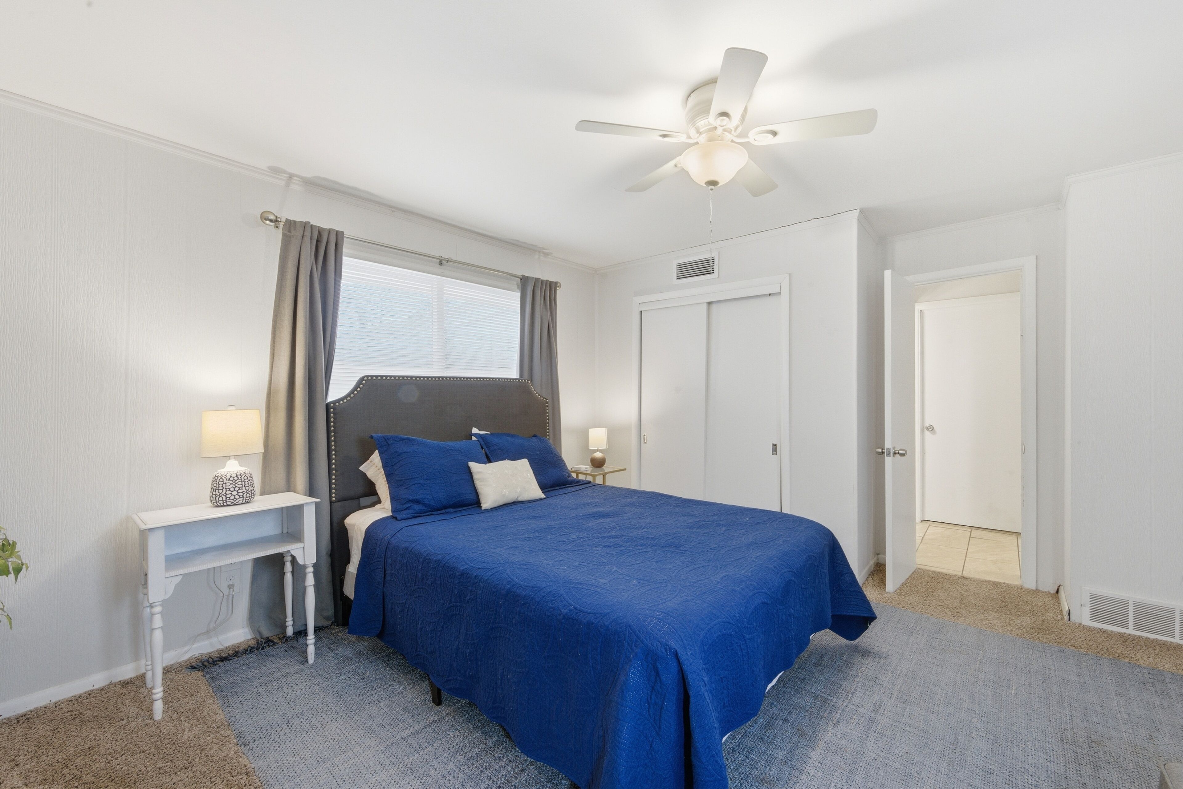 A bedroom with a bed, bedside tables, a ceiling fan, and a window with curtains.