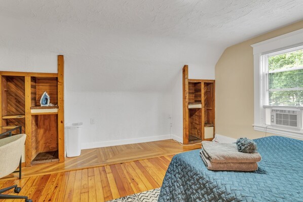 A bedroom with wooden built-in wardrobes, a bed with a blue quilt, and a window with blinds.
