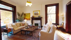 A living room with a sofa, armchair, coffee table, fireplace, and large windows. - Louisville Bourbon Inn (Louisville)