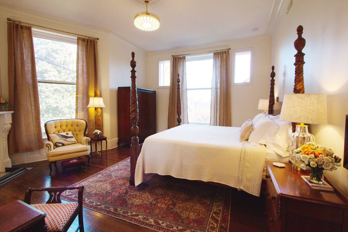 A hotel room with a large bed, a chair, a nightstand, and a window with curtains.