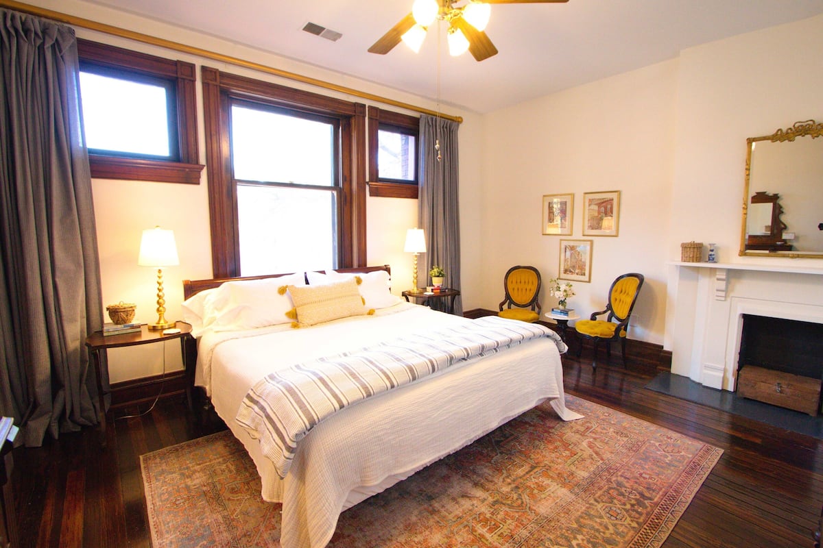 A hotel room with a large bed, a fireplace, a wooden floor, and a ceiling fan.