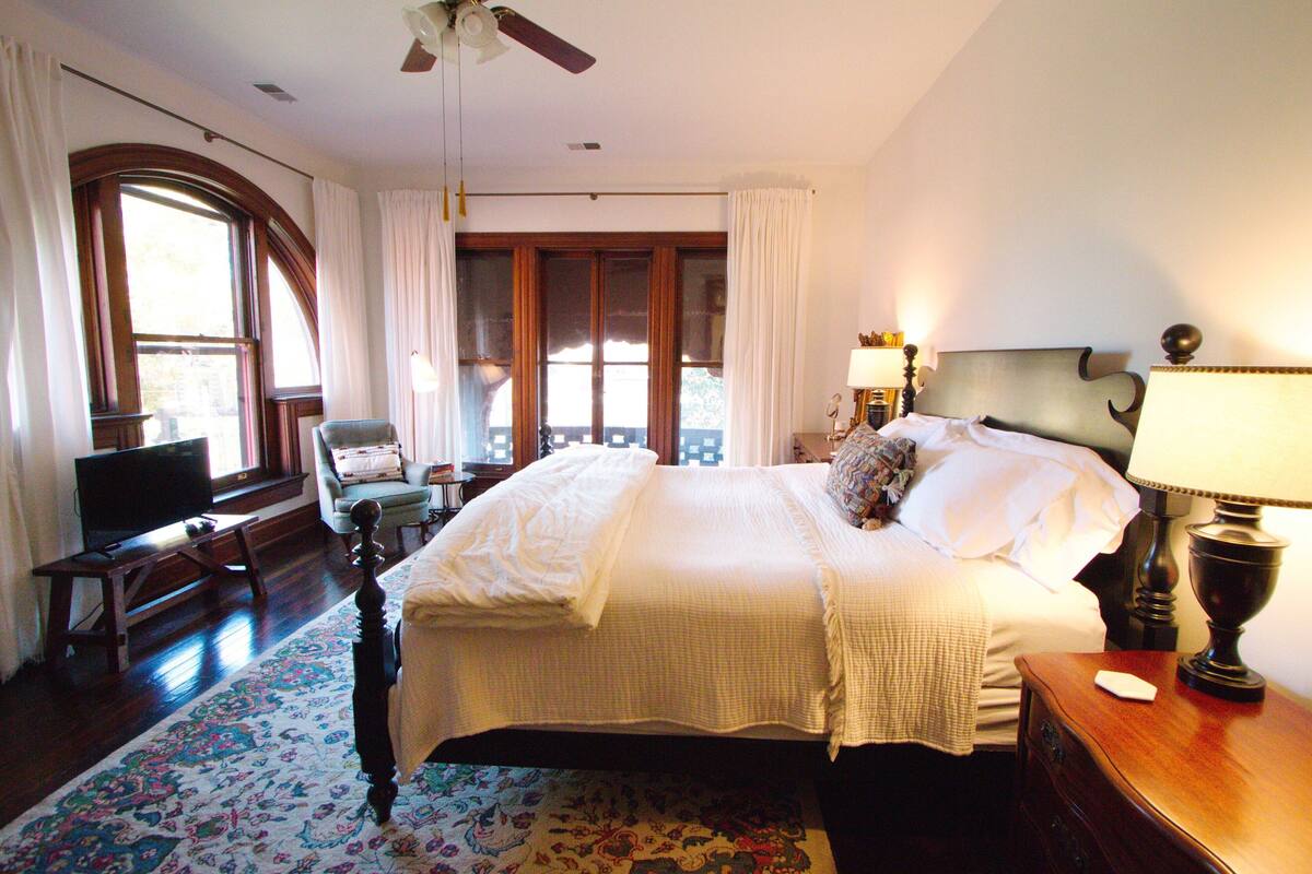 A hotel room with a large bed, a desk with a computer, a chair, and a window with curtains.