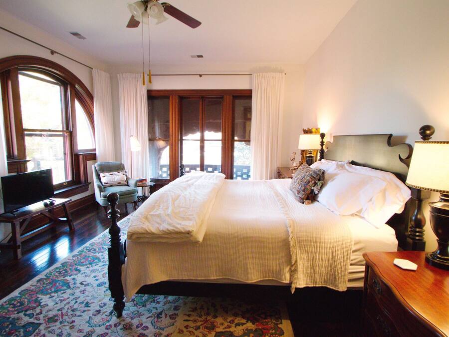 A hotel room with a large bed, a desk with a computer, a chair, and a window with curtains.
