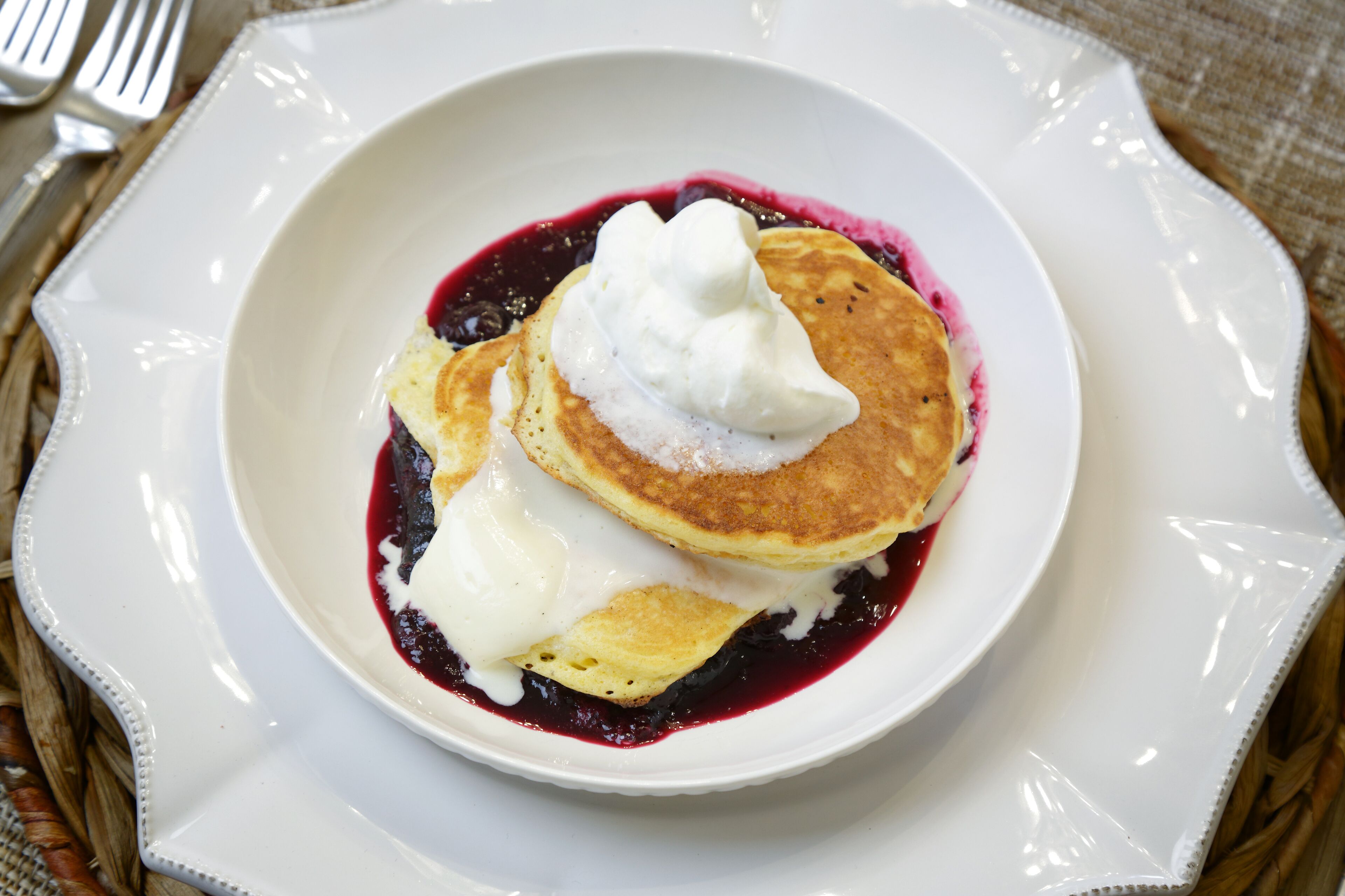 A plate of pancakes with whipped cream and blueberry sauce.