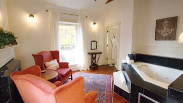 A room with a large window, a sitting area with chairs, a small table, and a bathroom with a bathtub.