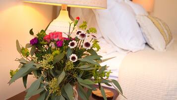 Une table de chevet avec un vase de fleurs, une lampe et un lit recouvert de linge de lit blanc.
