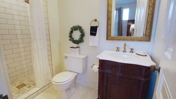 Une salle de bain avec des toilettes blanches, une douche avec un rideau blanc, un lavabo avec un robinet doré et un miroir avec un cadre doré.