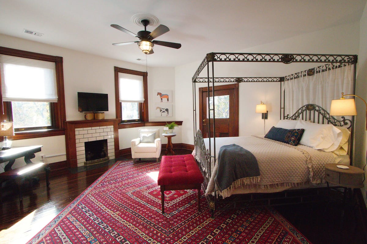 A bedroom with a four-poster bed, a fireplace, a television, and a large rug.