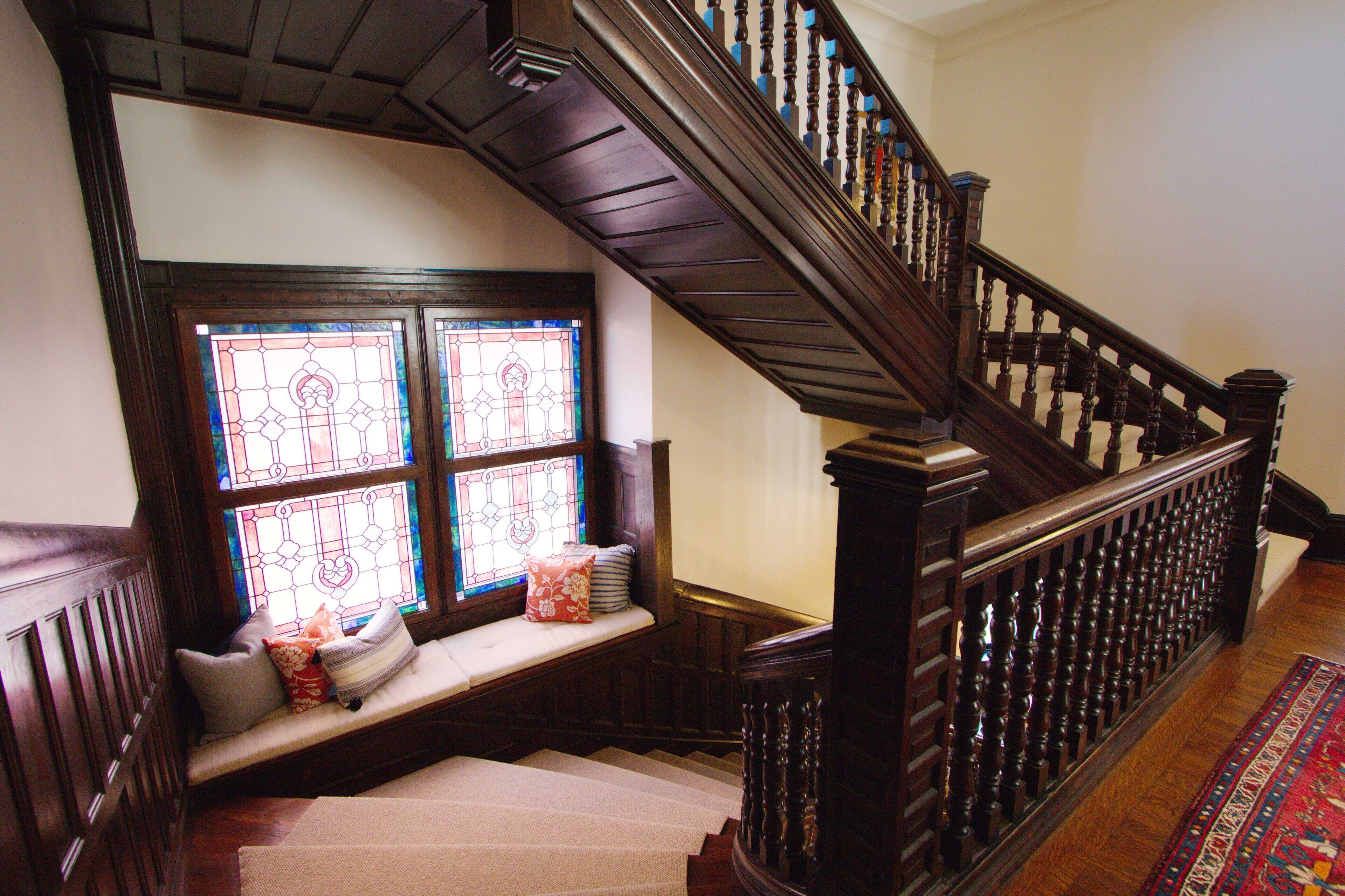 A wooden staircase with a handrail, a stained glass window, and a bench with cushions.