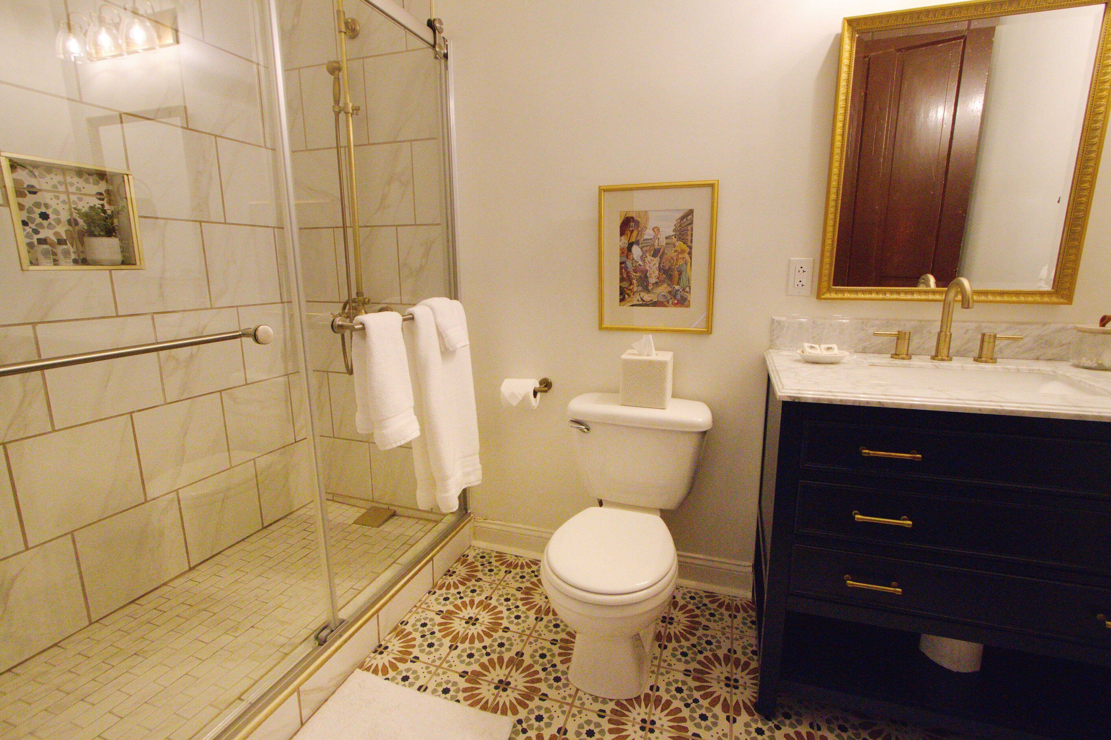 Une salle de bain dotée d’une douche à parois de verre, de toilettes, d’un lavabo avec un robinet doré et d’un meuble-lavabo foncé avec des tiroirs.