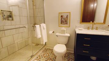 Une salle de bain dotée d’une douche à parois de verre, de toilettes, d’un lavabo avec un robinet doré et d’un meuble-lavabo foncé avec des tiroirs.