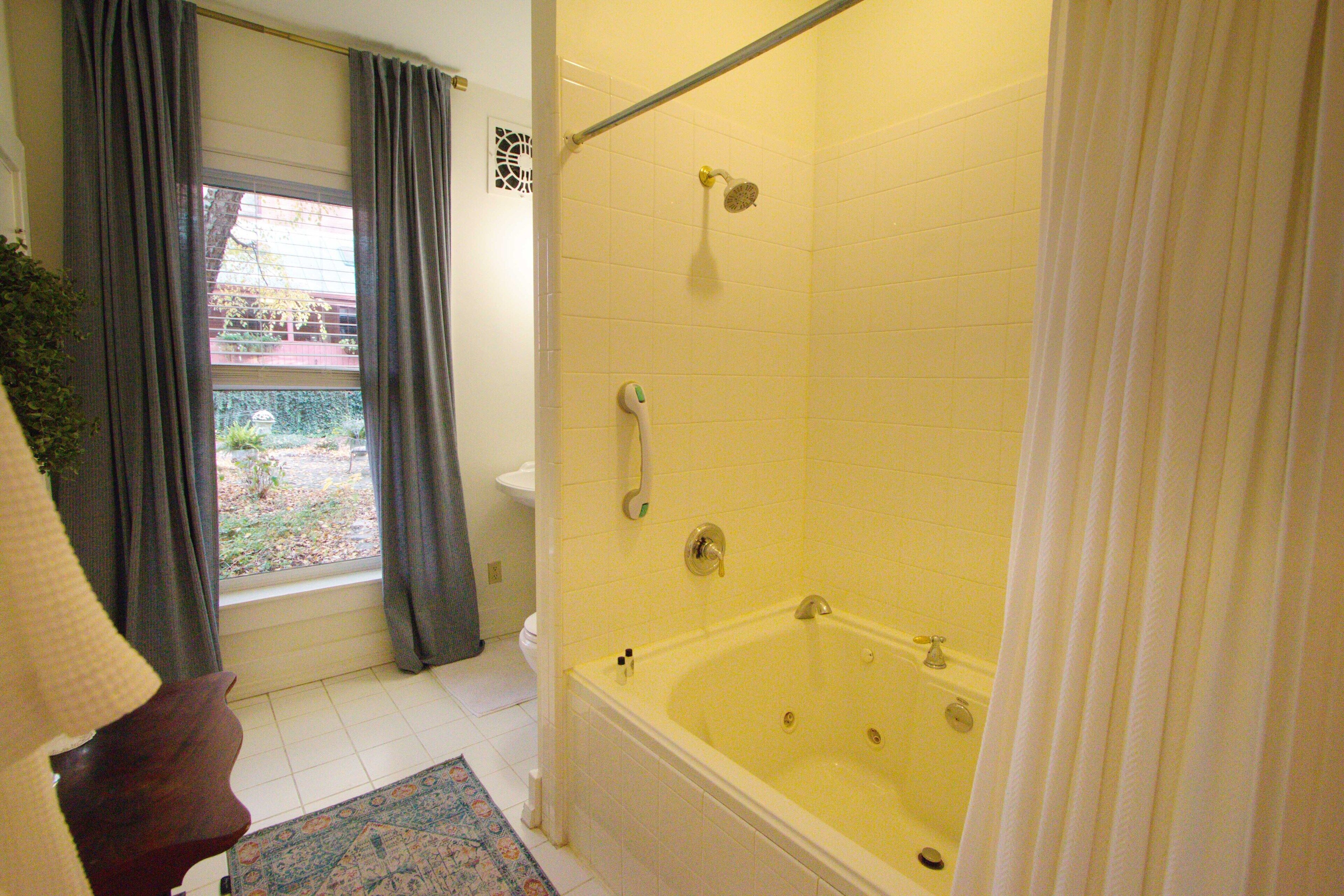 A bathroom with a bathtub, a shower, and a window with curtains.