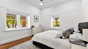 A bedroom with a large bed, two windows, a dresser, and a nightstand.