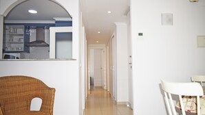 A hallway with a wicker chair and a white chair, leading to a kitchen area with a microwave and a stove. - Anacasa Medina Molins les Marines AP2201 (Denia)