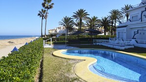 A swimming pool with a curved edge, surrounded by a well-maintained lawn and palm trees. - Anacasa Medina Molins les Marines AP2201 (Denia)