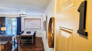Un comedor con una mesa y sillas de madera, una ventana con persianas y una puerta con pomo de latón.