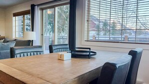 Un comedor con mesa de madera, sillas negras y ventana con persianas.