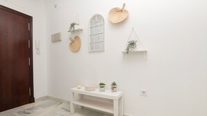 A room with a white wall, a wooden door, a white bench with decorative items, and wall-mounted shelves with woven baskets and plants.