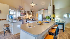 Una cucina moderna con isola centrale, sgabelli da bar, illuminazione a sospensione e vista sull'area pranzo.