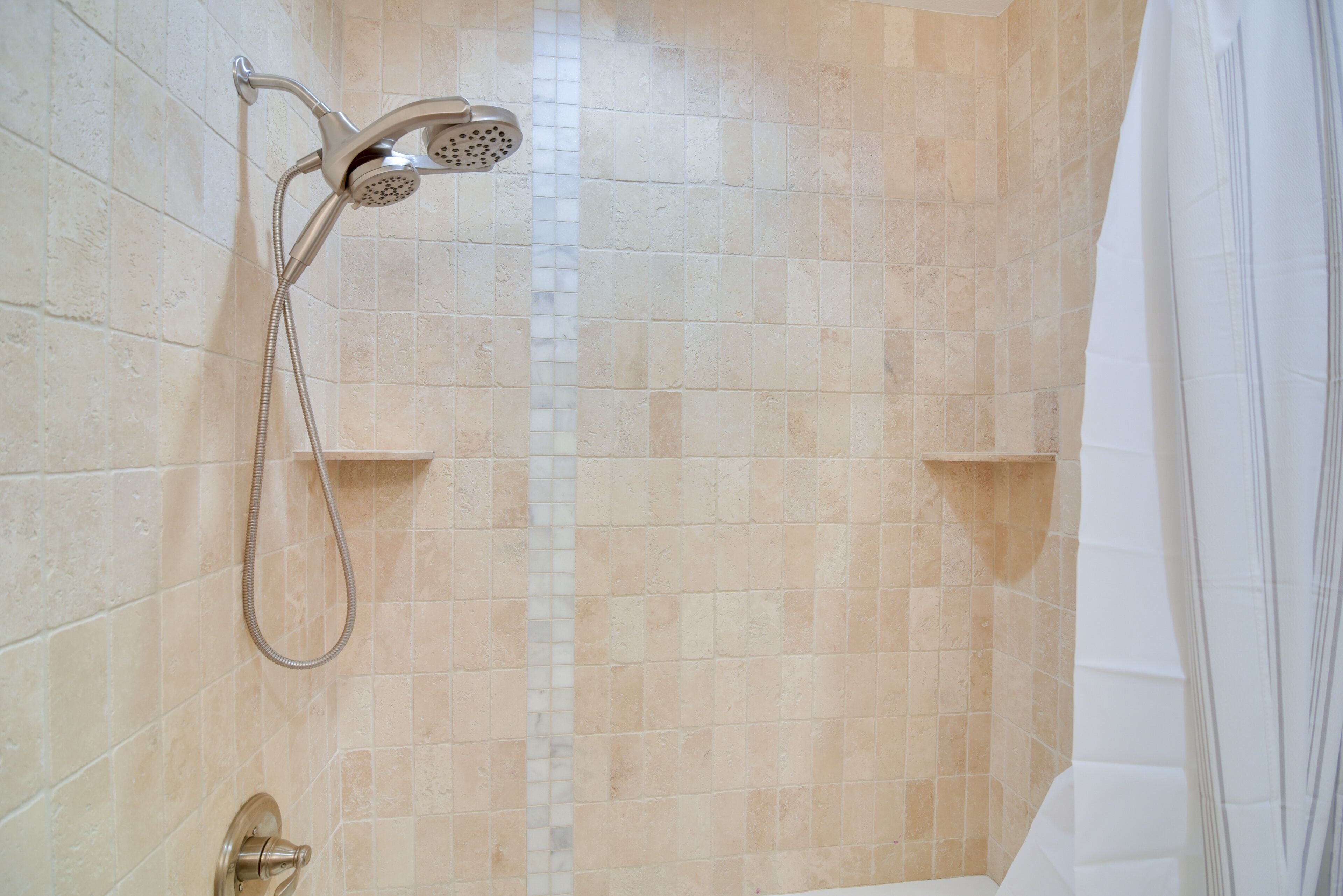 Una ducha con cabezal de ducha manual y grifo empotrado, con azulejos en tonos beige y blanco.