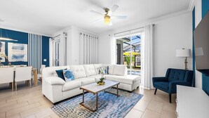 A modern living room with a white sectional sofa, a blue armchair, a coffee table, and a dining area with a white table and chairs.