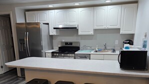 A modern kitchen with white cabinets, stainless steel appliances, and a central island with bar stools. - Crescent Bar Condos Unit 143 (Quincy)