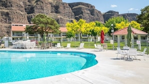 A swimming pool with lounge chairs and umbrellas, surrounded by a fence, with a mountainous backdrop. - Crescent Bar Condos Unit 143 (Quincy)