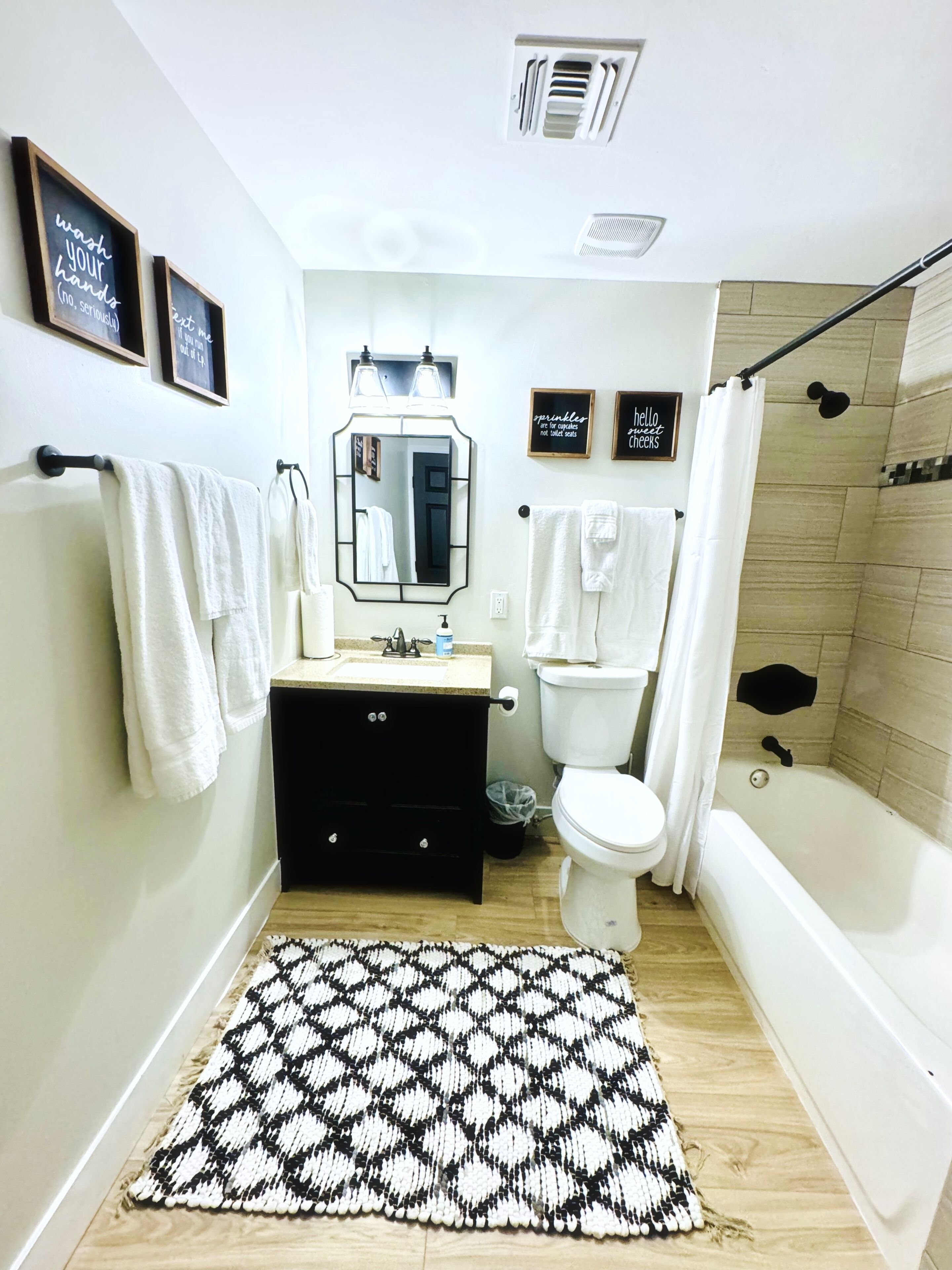 Un baño con un tapete blanco y negro estampado, un lavamanos blanco, un espejo, un inodoro y una bañera.