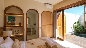 A hotel room with a bed, a bathroom visible through an archway, a sliding door to a balcony, and a sign on the wall. - Villa Koka Uluwatu (Pecatu)