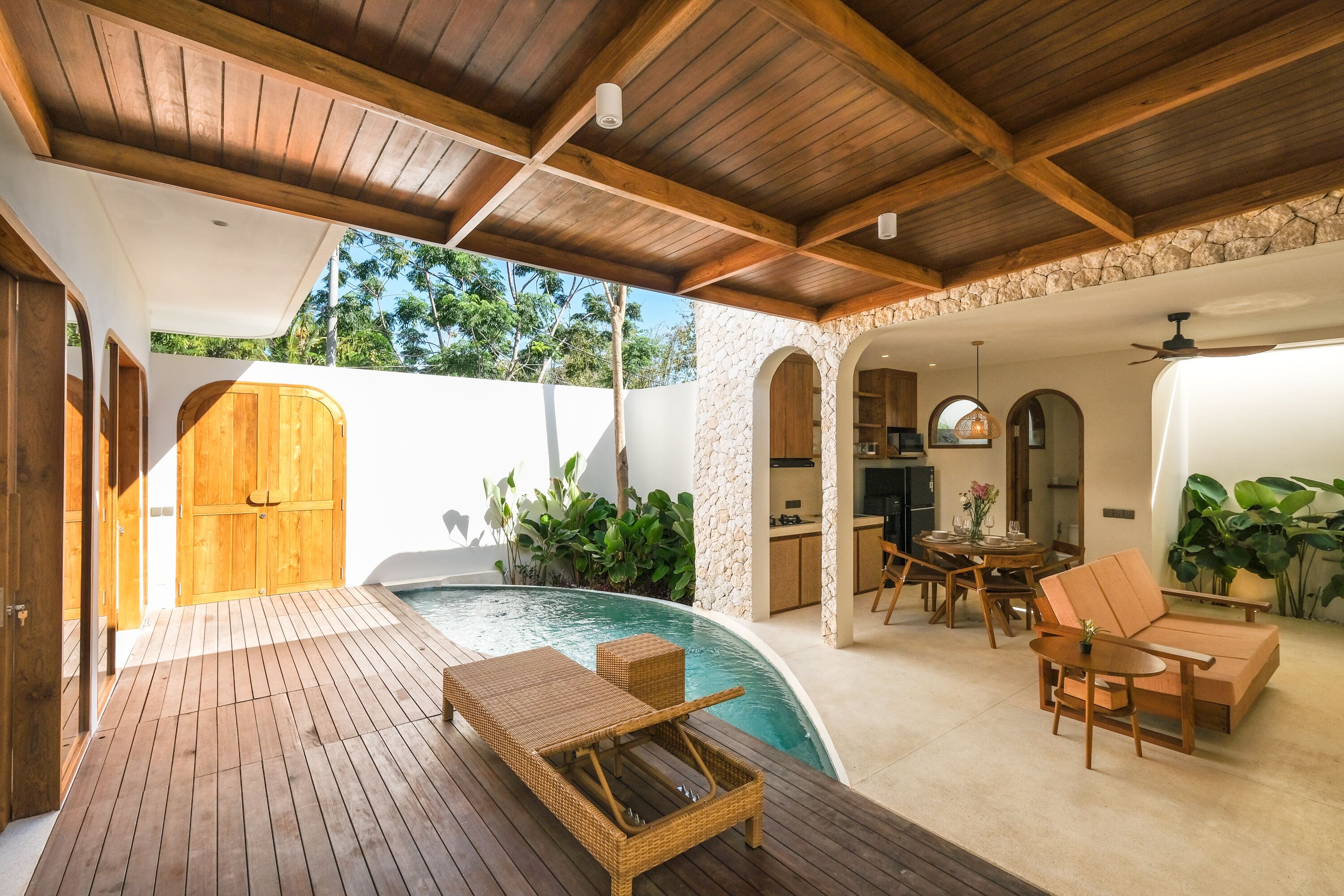 Um deck de madeira com piscina, móveis de exterior e uma parede de pedra.