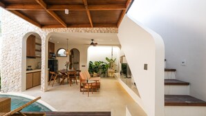 A spacious patio with a pool, wooden furniture, and a stone wall. - Villa Koka Uluwatu (Pecatu)
