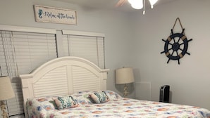 A bedroom with a white bed, a ceiling fan, a ship's wheel decoration, and a sign that says "Relax at the beach." - Coconut In Paradise Key largo (Key Largo)