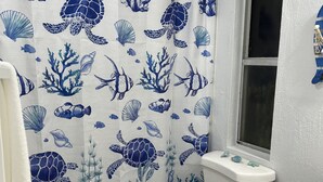 A bathroom with a white toilet, a shower curtain with a blue ocean theme, and a window. - Coconut In Paradise Key largo (Key Largo)